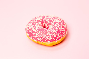 A donut in a pink glaze with a white sprinkles on a pink background. Sweets and desserts. Minimalistic background with clean place for the inscription. Copy space.