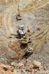 Heavy machinery excavators working on quarry and loading stone and granite into dump trucks. Bird...