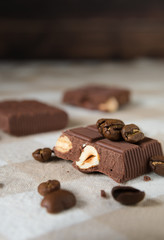 pieces of chocolate with hazelnuts and coffee beans on a brown tablecloth