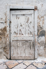 Old wooden door in a stone wall. Painted with white paint, cracks and damage on the textured surface.