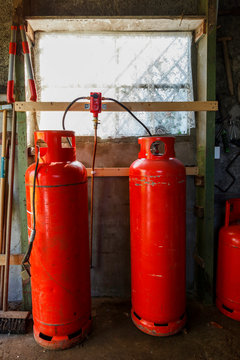2 large red gas bottles infront of a window, in an old shed.