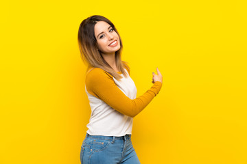 Pretty young woman over isolated yellow wall pointing back