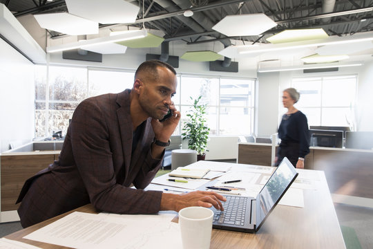 Mature Businessman Using Laptop On Phone In Office