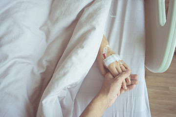 Close up of man hands holding his wife lover hand with saline intravenous at patient's bed in hospital. With Love and Caring