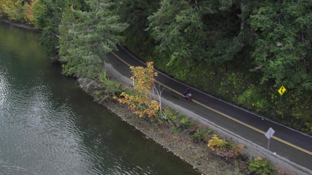 Aerial tracking shot of motorcycles riding through a forest next to water in Pacific Northwest