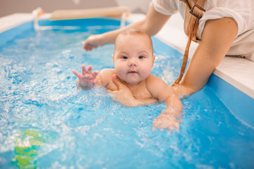 Fototapeta na wymiar Litle baby in pool swimming bathing during health procedures.