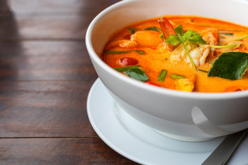 Tom Yam kung Spicy Thai soup with shrimp in white bowl on wood table. With copy space for text or design.