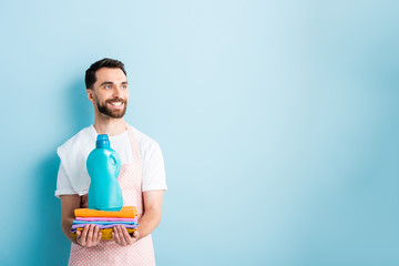 happy bearded man holding clean clothing and laundry detergent on blue - Powered by Adobe