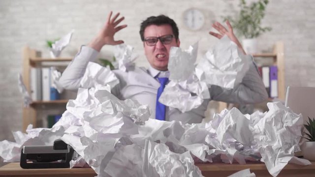 Screaming expressive man office worker in a heaps of office papers on the table slow mo