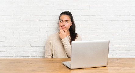 Young teenager Asian girl with a laptop in a table thinking an idea