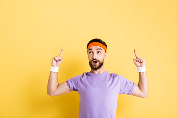surprised man in headband pointing with fingers on yellow