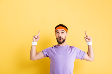Naklejka premium surprised man in headband pointing with fingers on yellow