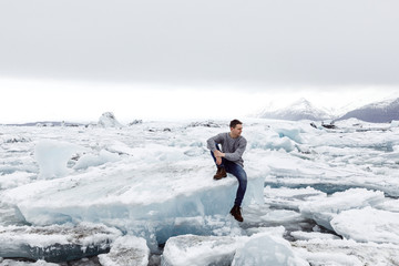 Fototapeta na wymiar young male traveler sits on an iceberg on an ice lake in Iceland
