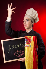 cuoca spagnola con bandiera e lavagna con su scritto paella