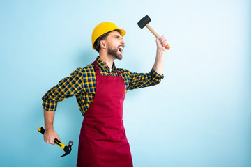 side view of angry workman holding hammers on blue