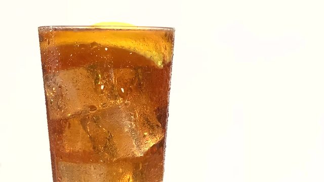 Drops on a rotating glass full of lemon ice tea and ice cubes. Ice cold tea in glass on a hot day. Isolated alcohol-free refreshment for hot days with white background.