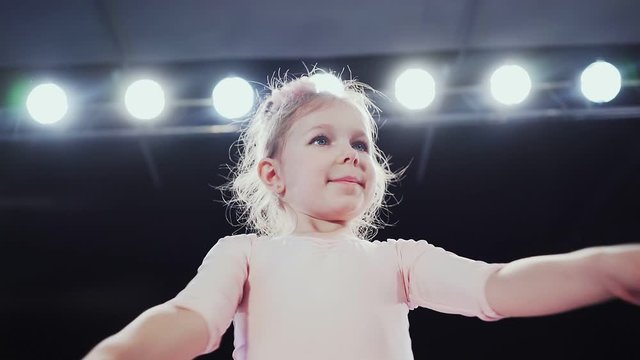 Baby girl in white tutu dancing on the stage. Little ballerina in the backlight. Slow motion