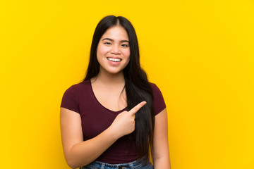 Obraz premium Young teenager Asian girl over isolated yellow background pointing finger to the side