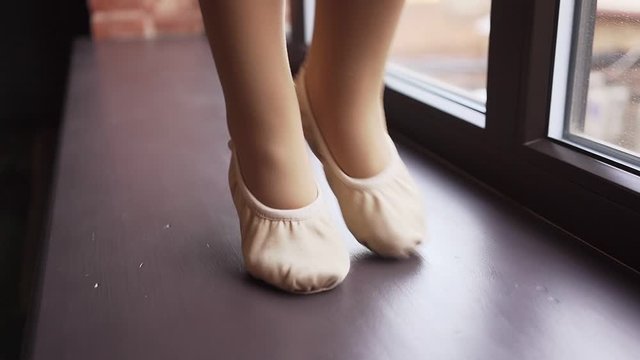 Little baby feet in ballet flats go along the window sill. Slow motion. Shooting on the Steadicam. Close up