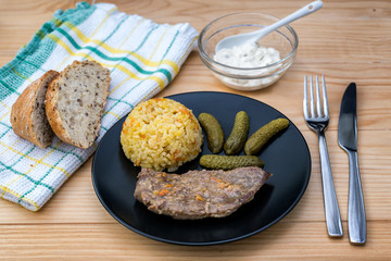 Prepared beef steak with rice risotto, pickles and sauce on black plate on wooden table background