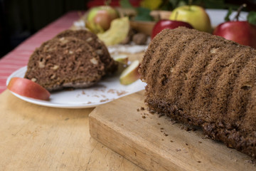 Sliced apple cinnamon bread with decorations on wooden table. Made from apples, sugar, oil, eggs, flour. Homemade apple loaf cake on plate with fresh apples and cinnamon in background at autumn