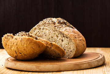 Loaf of wheat bread sprinkled with various seeds, with a cut slices of bread on a wooden table
