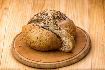 Loaf of wheat bread sprinkled with various seeds, with a cut slices of bread on a wooden table