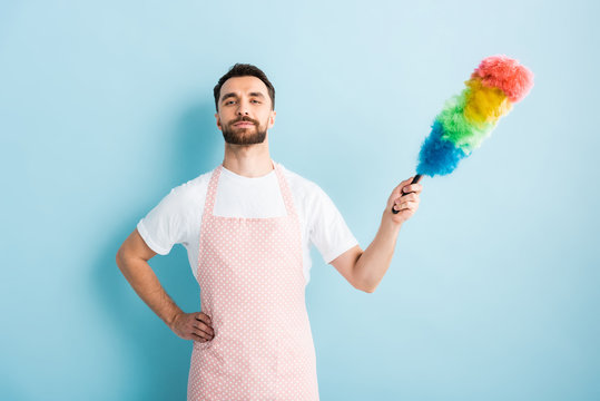 handsome man in apron holding dust brush on blue