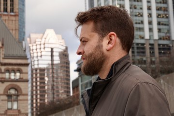Man with a beard smiling in downtown Toronto with sky rise buildings in the background