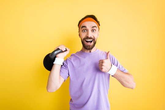 Cheerful Sportsman Holding Heavy Dumbbell And Showing Thumb Up Isolated On Yellow