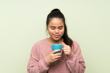 Fototapeta premium Young teenager Asian girl over isolated green background holding hot cup of coffee
