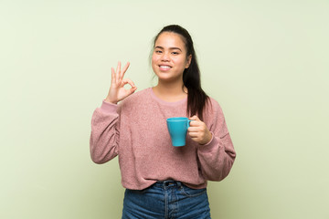 Young teenager Asian girl over isolated green background holding hot cup of coffee