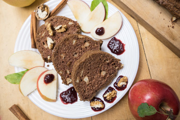 Sliced apple cinnamon bread with decorations on wooden table. Made from apples, sugar, oil, eggs, flour. Homemade apple loaf cake on plate with fresh apples and cinnamon in background at autumn