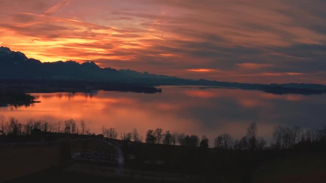 Anamorphic 4K Aerial Drone footage of a beautiful sunset with red clouds at the scenic Bavarian lake Chiemsee in southern Germany close to the mountains.