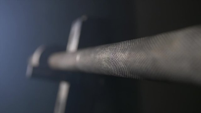 Close Up Of Unloaded Barbell On Squat Rack In Dark Dim Gym Room Industrial Gym Under Ground Gym. Smoke Rising Over And Filling Room With Cloudy Smoke Dark Grey Metal Extreme Focus On Pattern On Bar