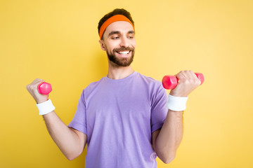 Fototapeta na wymiar cheerful sportsman exercising with small dumbbells isolated on yellow