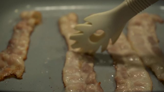 Bacon cooking and being flipped on skillet