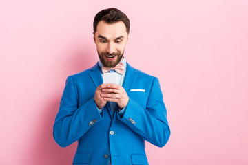 cheerful businessman using smartphone on pink