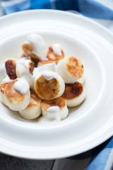 Close-up of fried vareniki or curd dumplings served with sour cream, selective focus, vertical shot