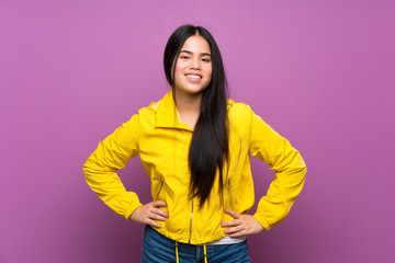 Young teenager Asian girl over isolated purple background posing with arms at hip and smiling