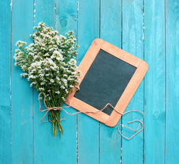 A bouquet of white cutter flower tied with rope and blackboard on light blue wooden background. Flowers composition. Flat lay. Copy space on blackboard.
