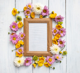 Blank photo frame and many flowers over white wooden background. Love cocept. Flowers composition. Flat lay. Copy space or photo on photo frame.