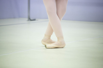  legs of a ballerina in white tights and beige pointes at a training session in the gym