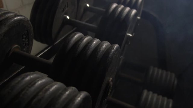 Close Up Pan Across Of Weights Lined Up On Weight Rack In Industrial Gym Old Style Old Fashioned Under Ground Gym. Paint Work Scratched Off Smoke Passing Over