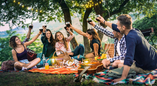 Happy friends having fun at vineyard on sunset - Young people millenial toasting at open air picnic under string light - Youth friendship concept with guys and girls drinking red wine at bar-b-q party