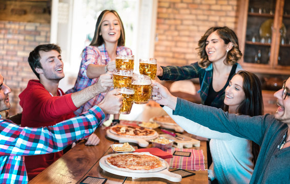 Friends group drinking beer and eating pizza at bar restaurant - Friendship concept with young people having fun together at risto pub pizzeria on happy hour - Focus on pint glasses - Warm filter
