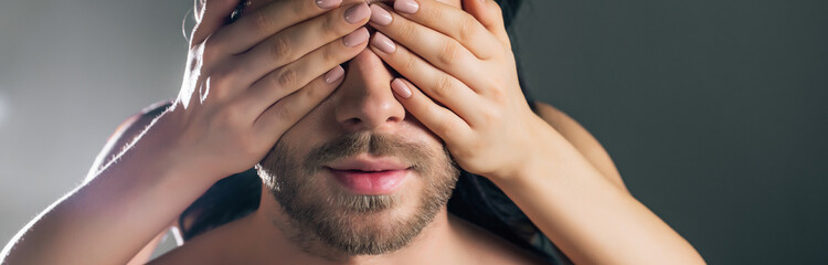 panoramic shot of girlfriend closing eyes of man on dark grey with back light