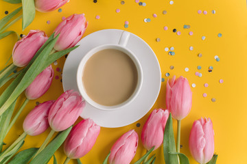 Cup of coffee with milk, bright tulips, confetti on yellow background. Birthday card concept.