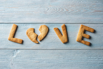 Word love from a sweet cookie in the shape of a broken heart on a blue wooden background. Romantic Valentine's day gift