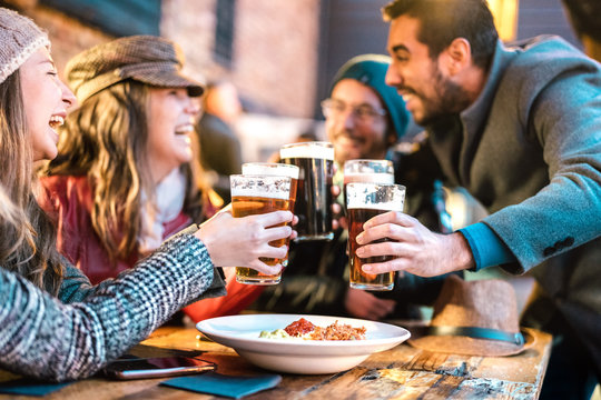 Friendly guys approaching happy girls at brewery pub outdoor on winter time - Friendship concept with young people having drunk fun together drinking beer at happy hour promotion - Vivid color filter